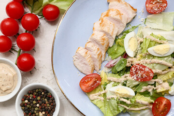 Plate of tasty chicken Caesar salad with tomatoes and bowl of peppercorn on white background, closeup