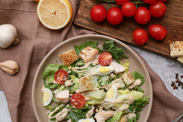 Plate with tasty chicken Caesar salad, lemon and garlic on grey background, closeup