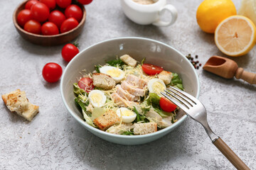Bowl with tasty chicken Caesar salad, tomatoes and lemons on grey background