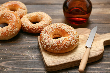 Cutting board of tasty bagels with sesame seeds on wooden background, closeup