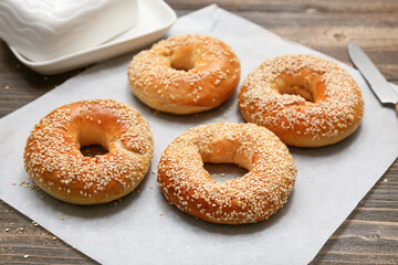 Baking paper of tasty bagels with sesame seeds on wooden background