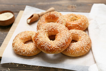 Baking paper of tasty bagels with sesame seeds on wooden background