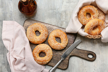 Wooden board and wicker bowl of tasty bagels with sesame seeds on grey background