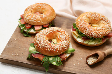 Wooden board of tasty bagel sandwiches with ingredients on white background, closeup