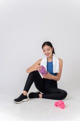 Fototapeta premium Healthy Asian woman in sportswear sits on a white studio background, holding a protein shake bottle.