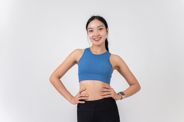 A confident, sporty Asian woman in sportswear smiling at the camera, standing on a studio background