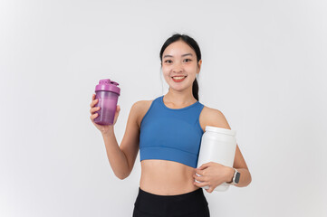 A confident, healthy Asian woman in sportswear holding a bottle and a bucket of a protein shake.