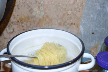 white enamel pot filled with boiling water and spaghetti metal spoon cooking tutorials home kitchen everyday food for the homeless charity efforts raising awareness healthy eating habits distribution