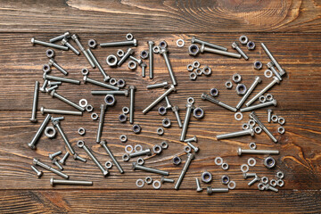 Tap bolts and chrome nuts on brown wooden background, closeup