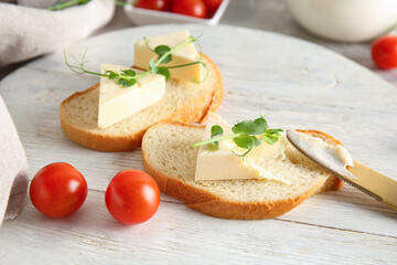 White wooden board of bread slices with triangles of tasty processed cheese and micro green on grey background