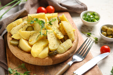 Wooden plate of tasty potato salad with pickled cucumber and tomatoes on white background