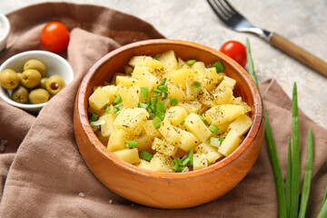 Wooden bowl of tasty potato salad with green onion and olives on grey background