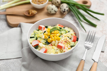 Bowl of salad with crab sticks, corn, cucumber and ingredients on light grunge background