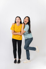 Two lovely, cheerful Asian female best friends standing against a white studio background.