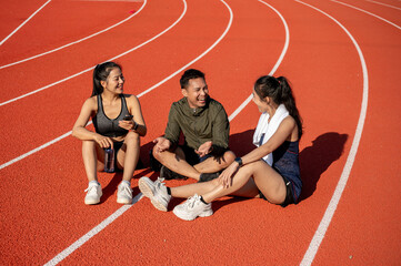 Portrait of a group of cheerful Asian athlete friends resting on a sports track after training.