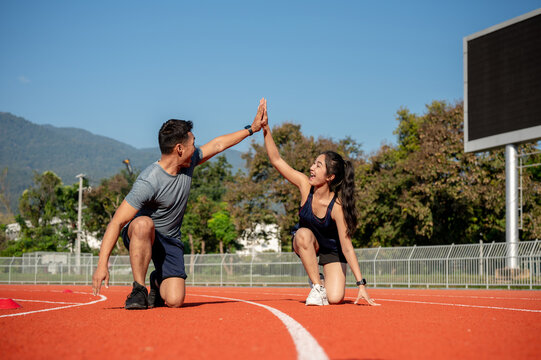 Two runners give high five while getting ready to run on a running track, training at a stadium
