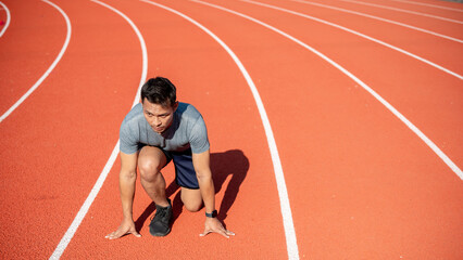 A strong Asian athletic male runner in sportswear trains at a stadium, preparing to run