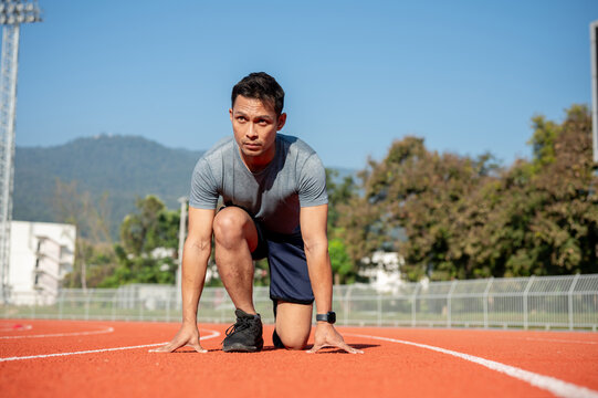 A strong Asian athletic male runner in sportswear trains at a stadium, preparing to run - Powered by Adobe