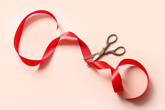 Red satin ribbon and scissors on pink background