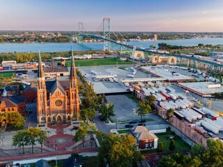 Aerial view of a bustling border crossing. Trucks line up for customs, while a city church and residential areas are visible. BASILICA OF SAINTE ANNE DE DÉTROIT, DETROIT, MICHIGAN, UNITED STATES