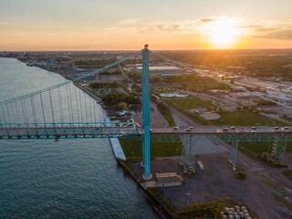 Aerial view of the Ambassador Bridge at sunset. Cars cross the bridge over the Detroit River. Cityscape and industrial area visible below. AMBASSADOR BRIDGE, DETROIT, MICHIGAN, UNITED STATES