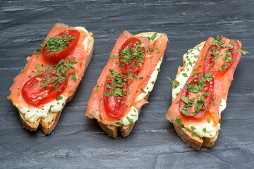 Salmon canape with tomato and cheese on black slate background