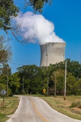Rural road winds past a power plant, steam rising from cooling towers. Sunny day, tranquil scene....