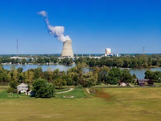 Panoramic view of a nuclear power plant, lake, and surrounding countryside. Smoke rises from the...