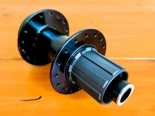 A black bicycle wheel is on a wooden surface. The wheel is missing its spokes and is not attached to a bicycle