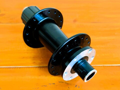 A black bicycle wheel is on a wooden surface. The wheel is missing its spokes and is not attached to a bicycle