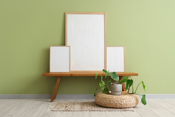 Blank posters on bench and houseplant  near green wall in living room