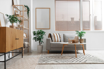 Cozy sofa, coffee table and chest of drawers with blank posters in interior of living room