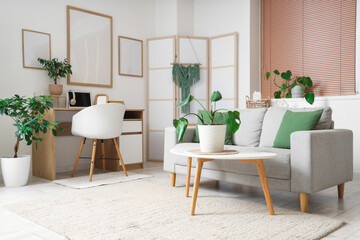 Cozy sofa, workplace with laptop and blank posters on white wall in room