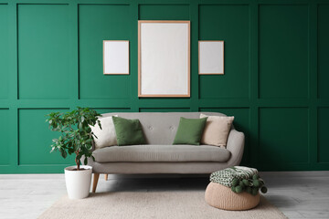 Cozy sofa, houseplant and blank posters on green wall in room