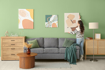 Young woman hanging picture on green wall in living room