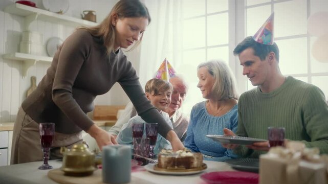 Happy family eating sweet cake in birthday party, woman cutting cake by knife. Celebrating anniversary and success, different aged persons enjoying joint pastime, unhealthy food, enjoying dessert