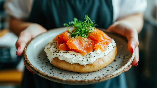 Chef holding plate with bagel, cream cheese, salmon, and dill