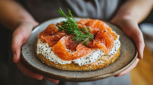 Chef holding plate with bagel, cream cheese, salmon, and dill