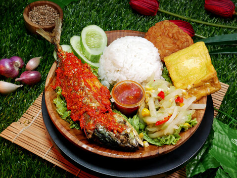Close up A complete meal featuring white rice, fried fish with red sambal, fried tempeh, fried tofu, fresh vegetables, sambal, and cucumber slices.