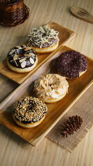 several donuts with chocolate topping, tiramisu, peanut cheese and sprinkles, on a wooden base, photographed with studio light with a wooden theme