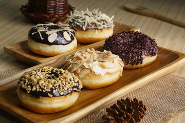 several donuts with chocolate topping, tiramisu, peanut cheese and sprinkles, on a wooden base, photographed with studio light with a wooden theme