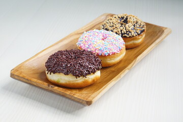 several donuts with chocolate topping, tiramisu, peanut cheese and sprinkles, on a wooden base, photographed with studio light with a wooden theme