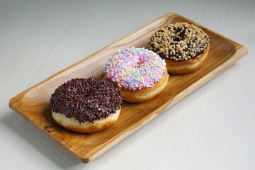 several donuts with chocolate topping, tiramisu, peanut cheese and sprinkles, on a wooden base, photographed with studio light with a wooden theme