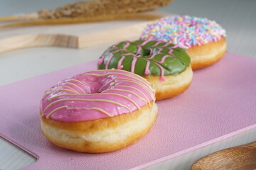 three donuts with strawberry matcha topping and sprinkles, on a pink plastic plate photographed with studio light