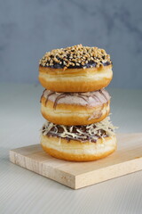 three medium sized donuts topped with chocolate sprinkles, tiramisu nuts and cheese, stacked together, on a wooden board photographed with studio light