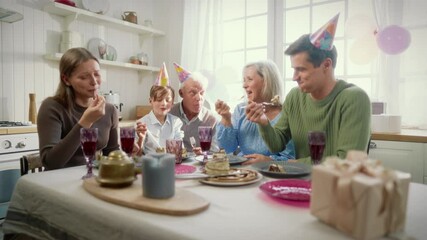 Caucasian family dining at home kitchen, eating birthday cake and smiling. Cheerful people of three generations enjoying delicious cake and chatting joyfully, spending merry time together in weekend