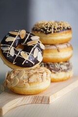 three medium sized donuts topped with chocolate sprinkles, tiramisu nuts and cheese, stacked together, on a wooden board photographed with studio light