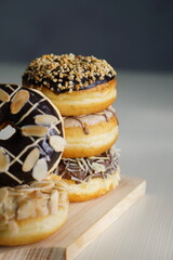 three medium sized donuts topped with chocolate sprinkles, tiramisu nuts and cheese, stacked together, on a wooden board photographed with studio light
