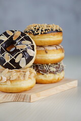 three medium sized donuts topped with chocolate sprinkles, tiramisu nuts and cheese, stacked together, on a wooden board photographed with studio light