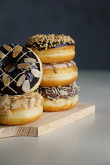 three medium sized donuts topped with chocolate sprinkles, tiramisu nuts and cheese, stacked together, on a wooden board photographed with studio light